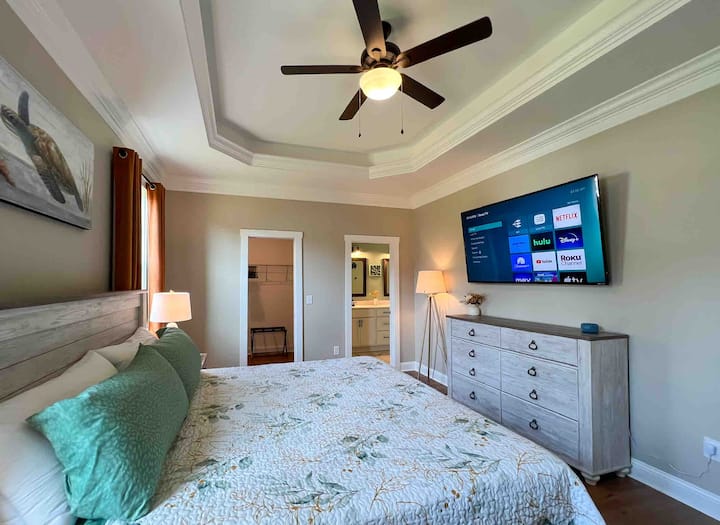 The room is equipped with a king size bed, two nightstands with electric + USB charging ports. Reading lamps, large dresser, and wall mounted 65” smart Roku TV.