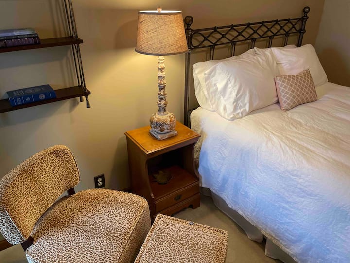 Chumba cha kwanza cha kulala kina kitanda aina ya queen na kiti cha kupendeza, cha kuchapisha chui na ottoman na kabati moja.