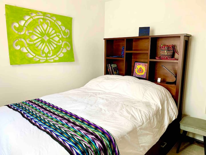 The green room features a full-sized Captain's bed with bookcase headboard, a ceiling fan, a closet with dresser drawers, and a beautiful painted stencil used to make the colorful sawdust carpets (alfombras) during Lenten processions.