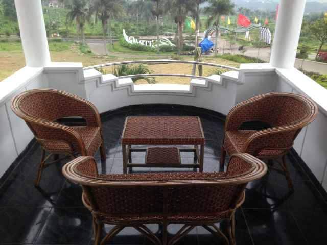 An outdoor balcony is furnished with four wicker chairs arranged around a small table. The space is enhanced by a surrounding view of greenery and flags in the distance, creating a calm atmosphere for relaxation.