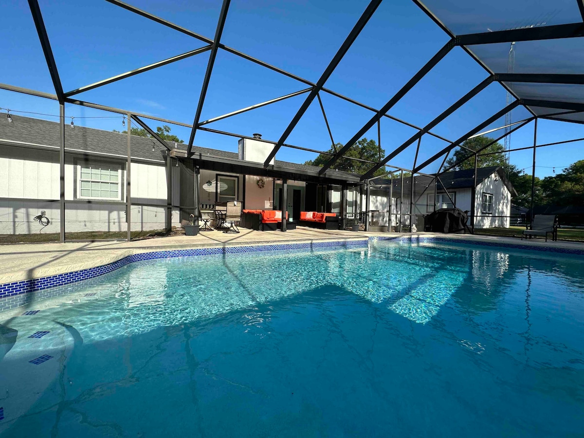 A screened-in outdoor area features a clear blue saltwater pool, showcasing a deep end. Sun loungers are positioned around the pool, with a patio area visible in the background. The space is brightened by natural light, providing a relaxed setting.