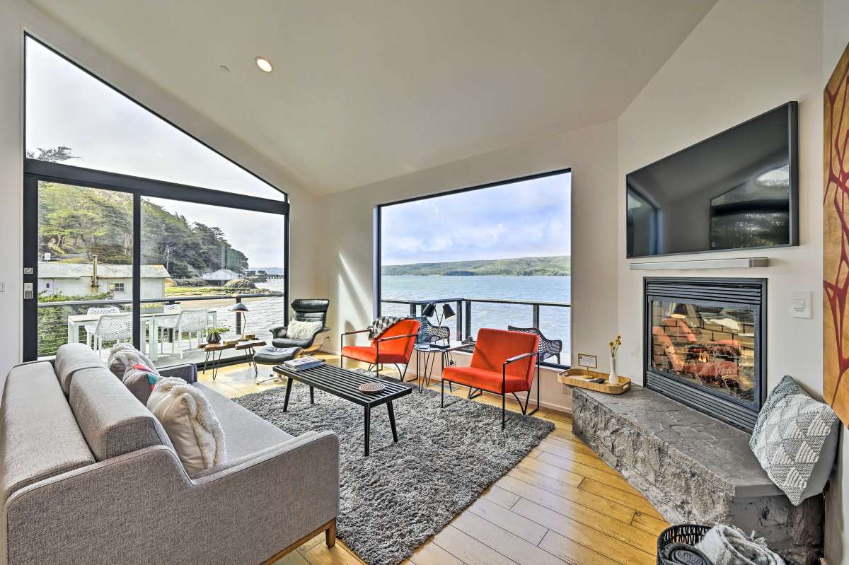 A modern living space is highlighted by large windows providing unobstructed views of the bay. A comfortable sectional sofa and vibrant chairs are arranged around a sleek coffee table. A gas fireplace and a wall-mounted television offer additional elements of comfort and utility.