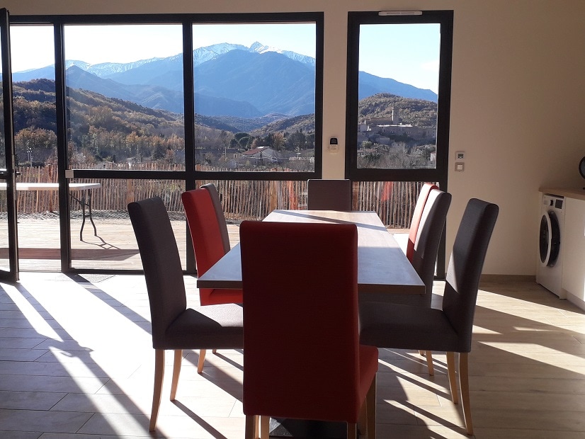A bright dining area is showcased with a large table surrounded by six chairs, offering ample space for gatherings. Expansive windows provide a wide view of the mountains, allowing natural light to fill the space while revealing the picturesque landscape outside.