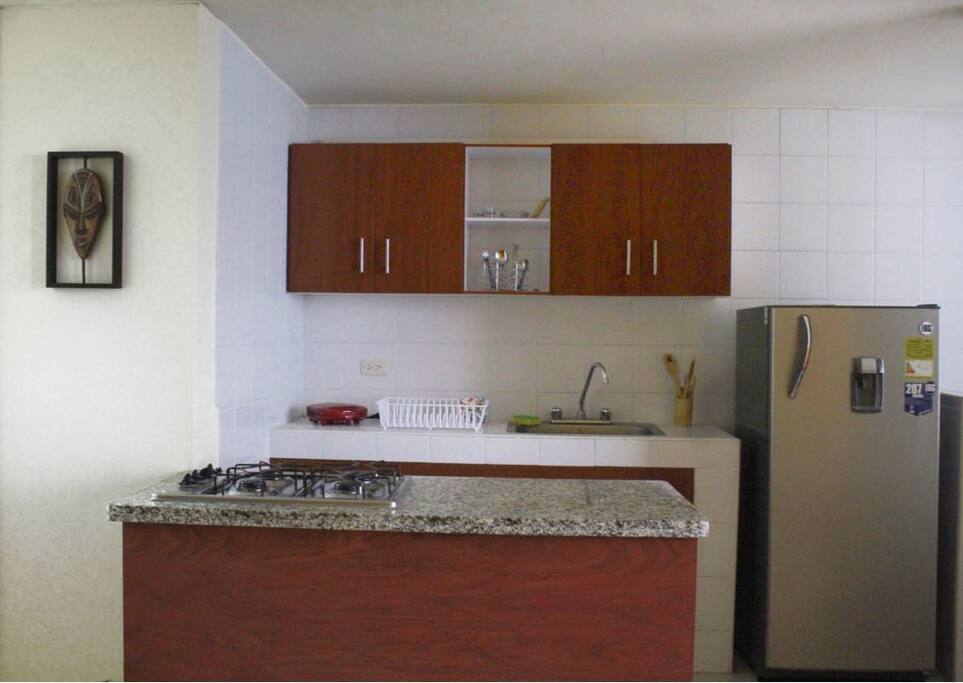 Cocina con nevera, estufa, sanduchera y todos los utensilios necesarios para cocinar.