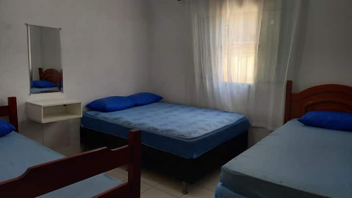 Dormitorio como una cama doble y una cama individual, con nicho de madera y espejo, ventilador de mesa.