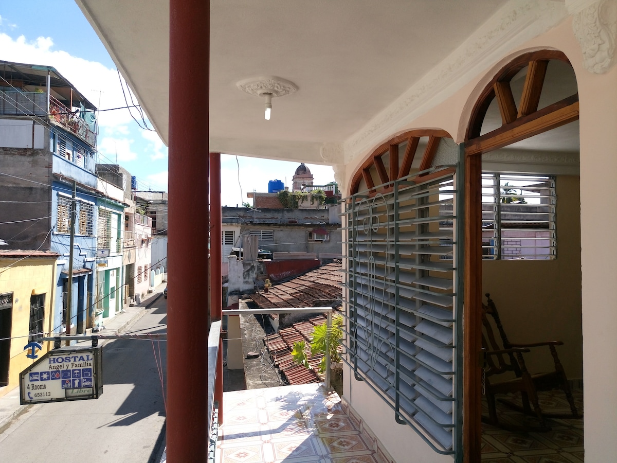 A spacious terrace is visible, featuring a rocking chair and offering views of the surrounding buildings and streets. Large windows allow natural light to enter the indoor space. The terrace flooring is tiled, enhancing the outdoor experience.
