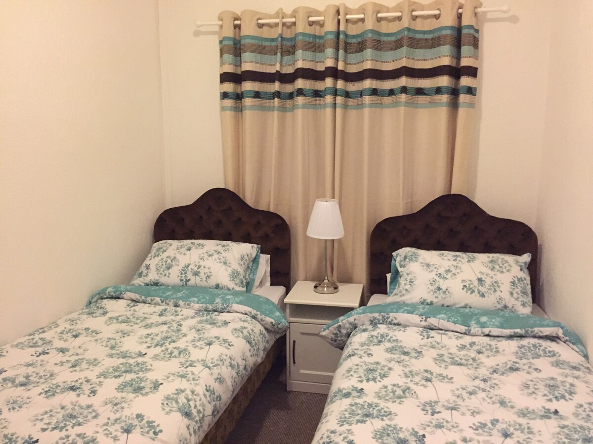 חדר שינה זוגי עם שידה וארון בגדים.  יש הרבה שקעים חשמליים זמינים לכל מיטה. 