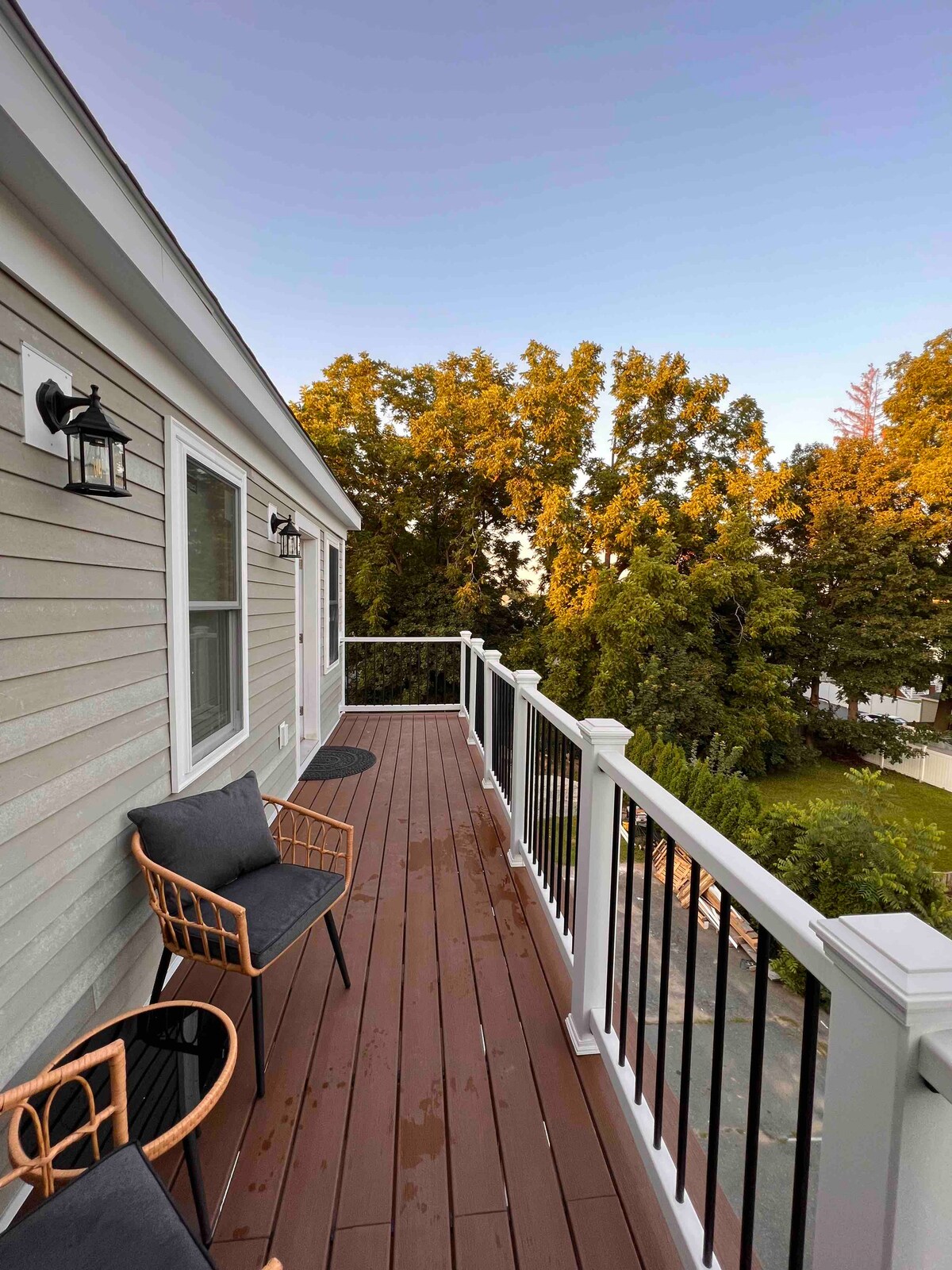 A private balcony features two seating areas, one with black chairs and the other with a round table. The view includes green trees and a serene outdoor space, creating a comfortable spot to enjoy nature.