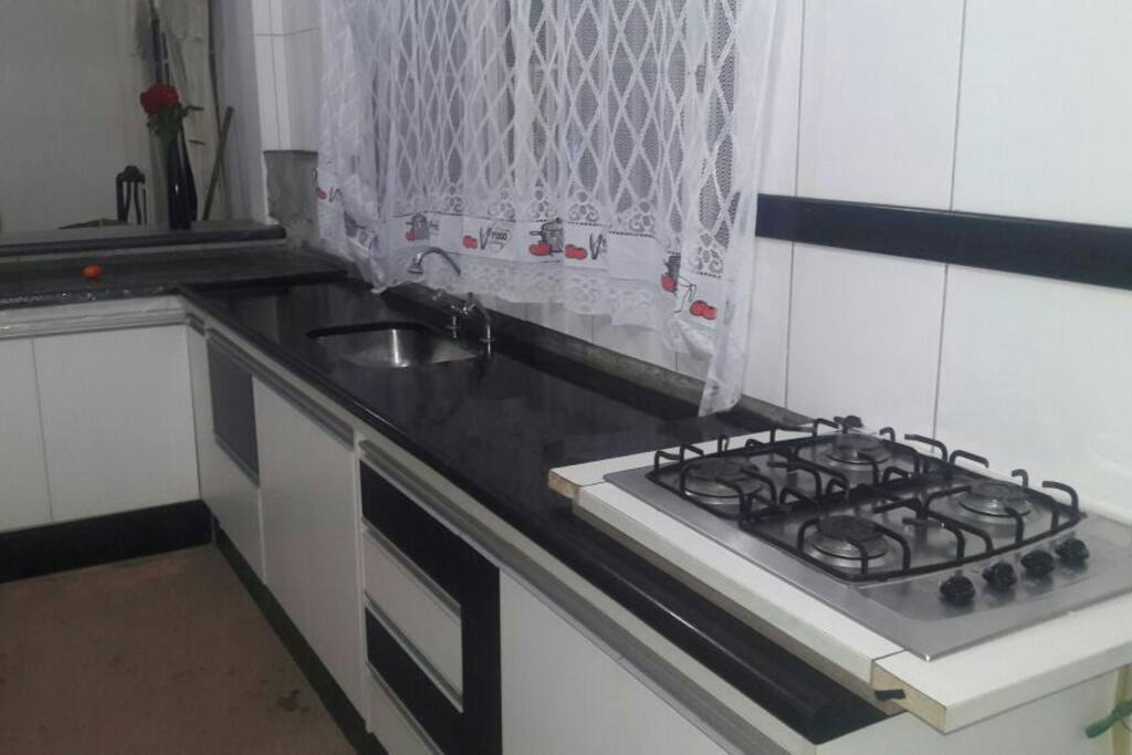 cozinha com balcão americano, pia ampla, fogão, armários embutidos, talheres, panelas, grill. forno elétrico, balcão marmorizado preto, fogão coocktop.