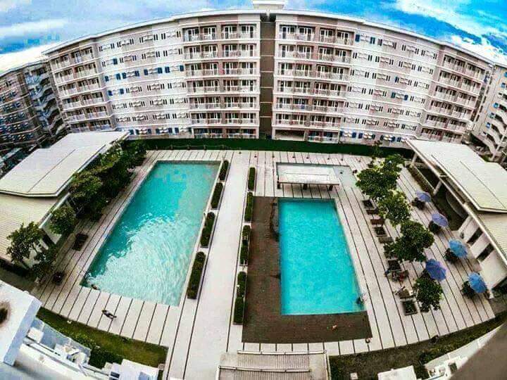 Two swimming pools are positioned within a well-maintained outdoor area, surrounded by neatly arranged greenery and lounge chairs. The layout allows for clear walkways alongside the pools, with multiple trees and umbrellas offering shaded spots for relaxation.