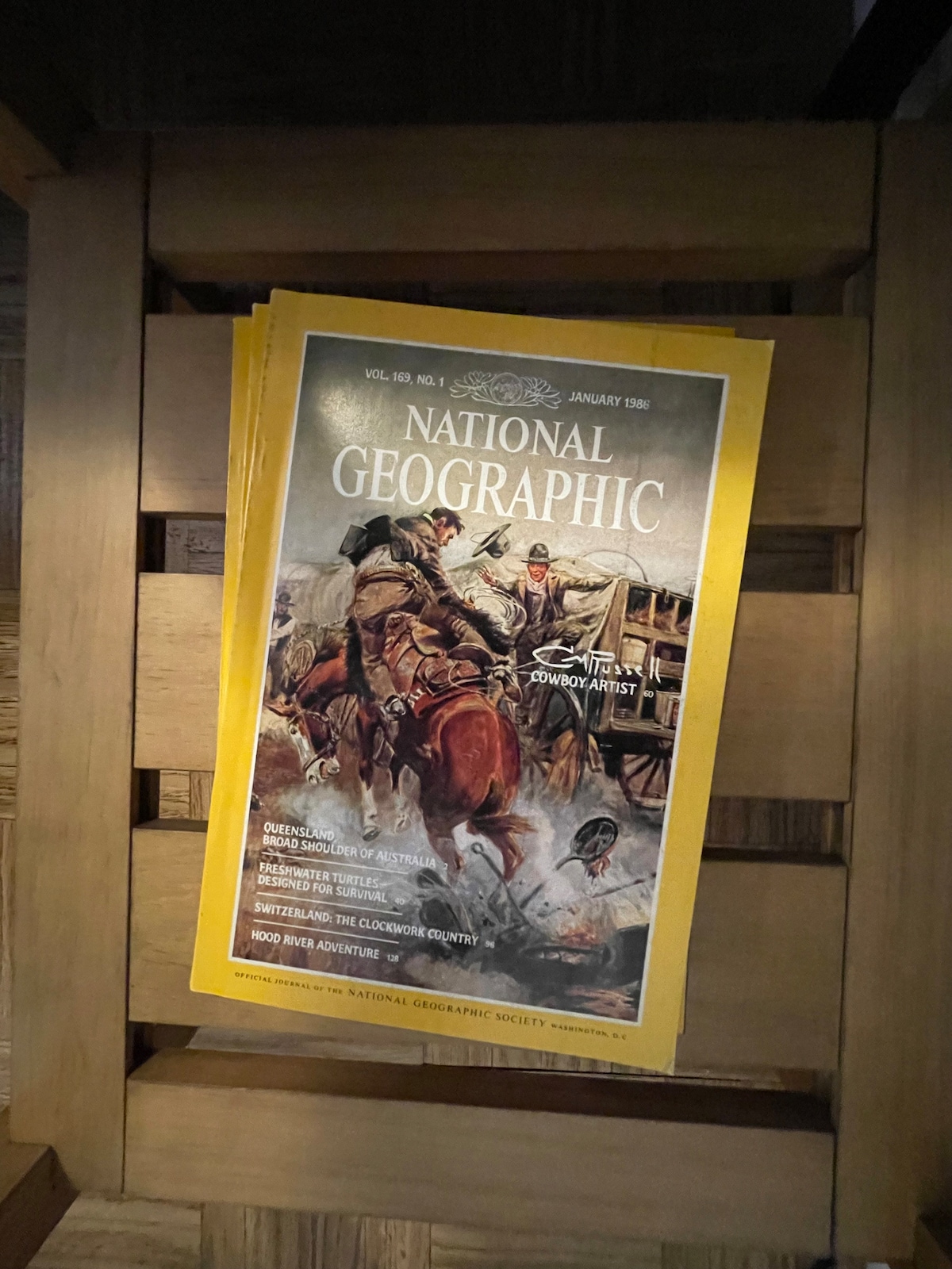 A stack of vintage National Geographic magazines is arranged neatly on a wooden surface. The cover of the January 1986 edition features colorful artwork, displaying a dynamic historical scene with characters on horseback. The yellowed edges of the pages add to its nostalgic appeal.