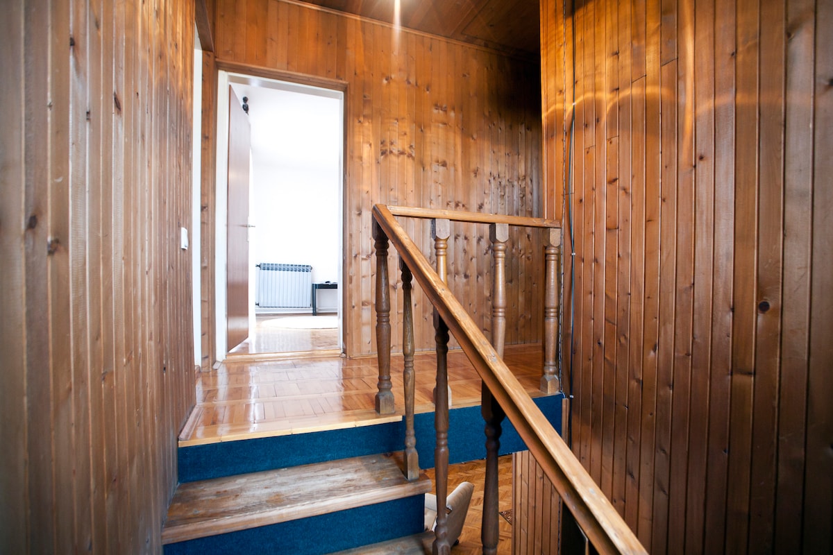 A staircase with wooden railings leads to a landing area with wood-paneled walls. The floor is finished in a warm tone, and a doorway is visible at the end, indicating access to another room that receives natural light.