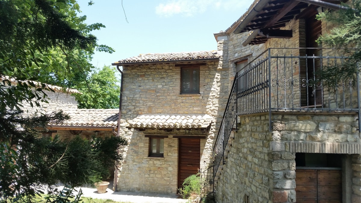 An exterior view of the rustic stone building features a sloped roof and wooden balconies. Surrounding greenery enhances the natural setting, and a pathway leads to the entrance. The structure reflects traditional architecture with its warm stone facade.