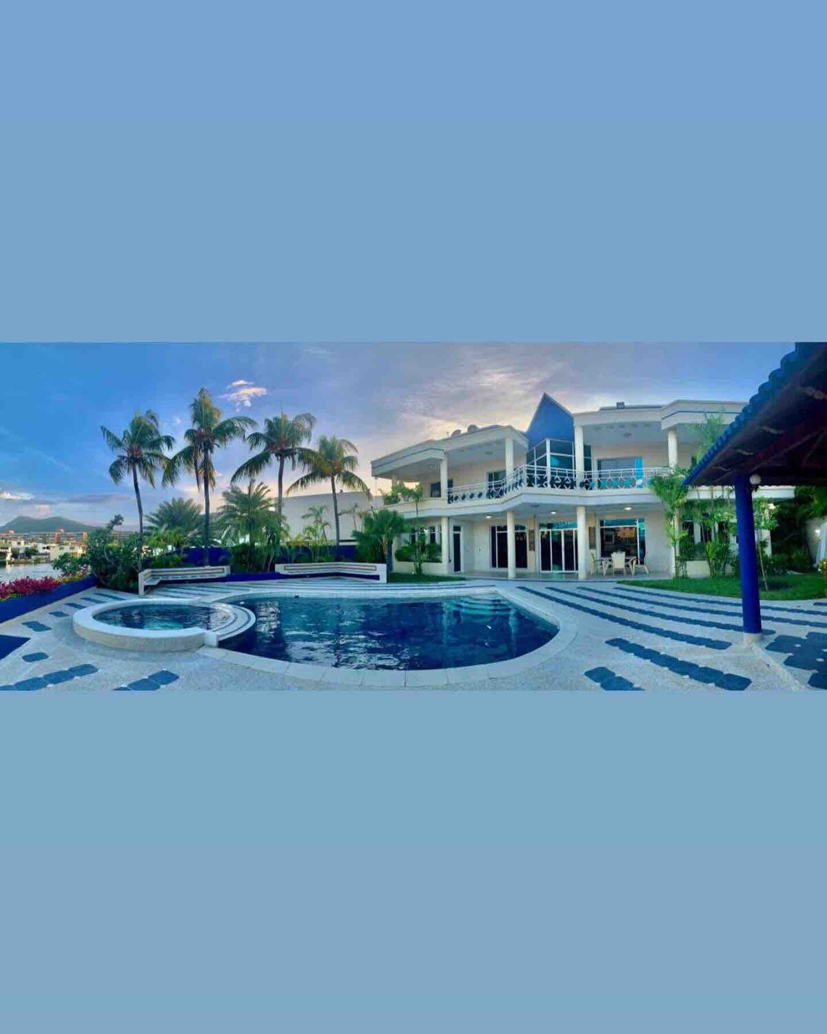 The luxurious villa is set against a backdrop of palm trees and a serene pool. A hot tub is positioned beside the large swimming pool, while the spacious terrace features patterned tiles. The structure showcases multiple levels with expansive windows reflecting the tranquil surroundings.