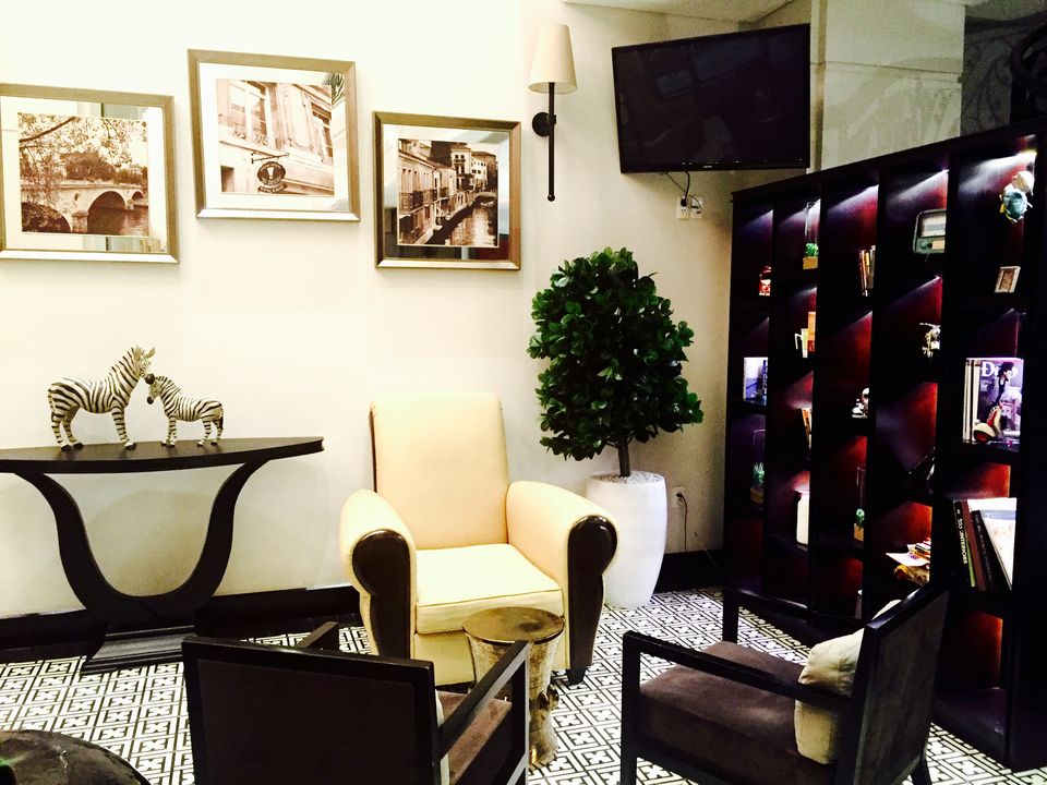 A comfortable seating area is present, featuring a light yellow armchair and dark wood chairs. A decorative console table displays two zebra figurines, while framed pictures adorn the walls. A bookshelf filled with books adds character to the space, enhanced by soft lighting.