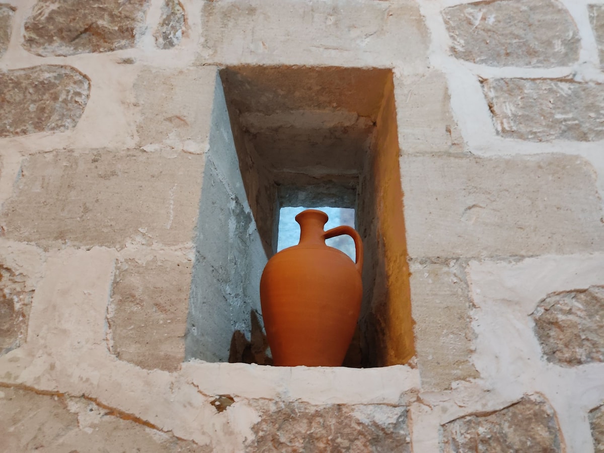 A traditional terracotta pot is displayed in a niche within the stone wall, showcasing the rustic charm of the dwelling's architecture. The natural textures of the stone enhance the warm tones of the pot, creating a harmonious blend of materials.