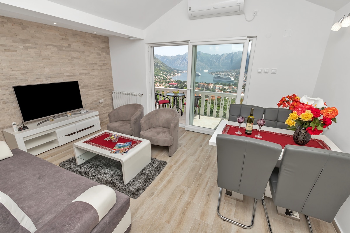 The living area showcases a modern design with a comfortable sofa and two armchairs. A dining table for four is set near the balcony, where guests can enjoy the bay view. A flat-screen TV is positioned across from the seating area, enhancing relaxation.