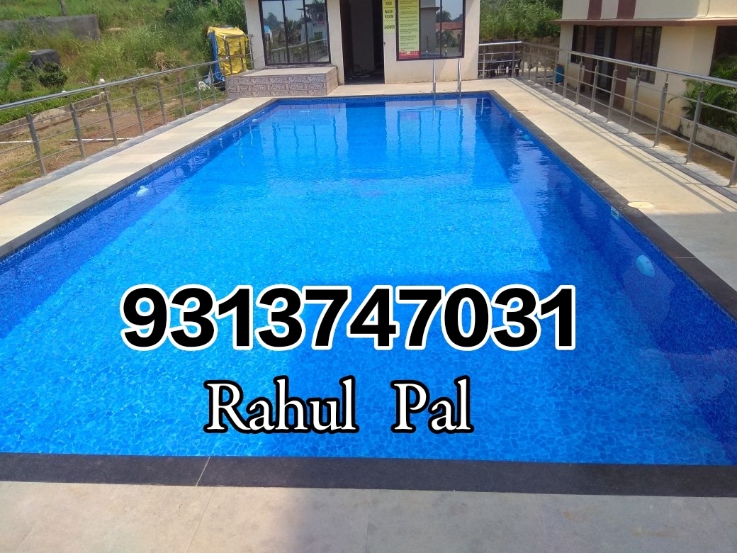 A clear blue swimming pool rests on a tiled patio, surrounded by a railing and lush greenery. The pool's surface reflects the light, creating a inviting atmosphere. In the background, a building features large glass doors that provide access to the pool area.