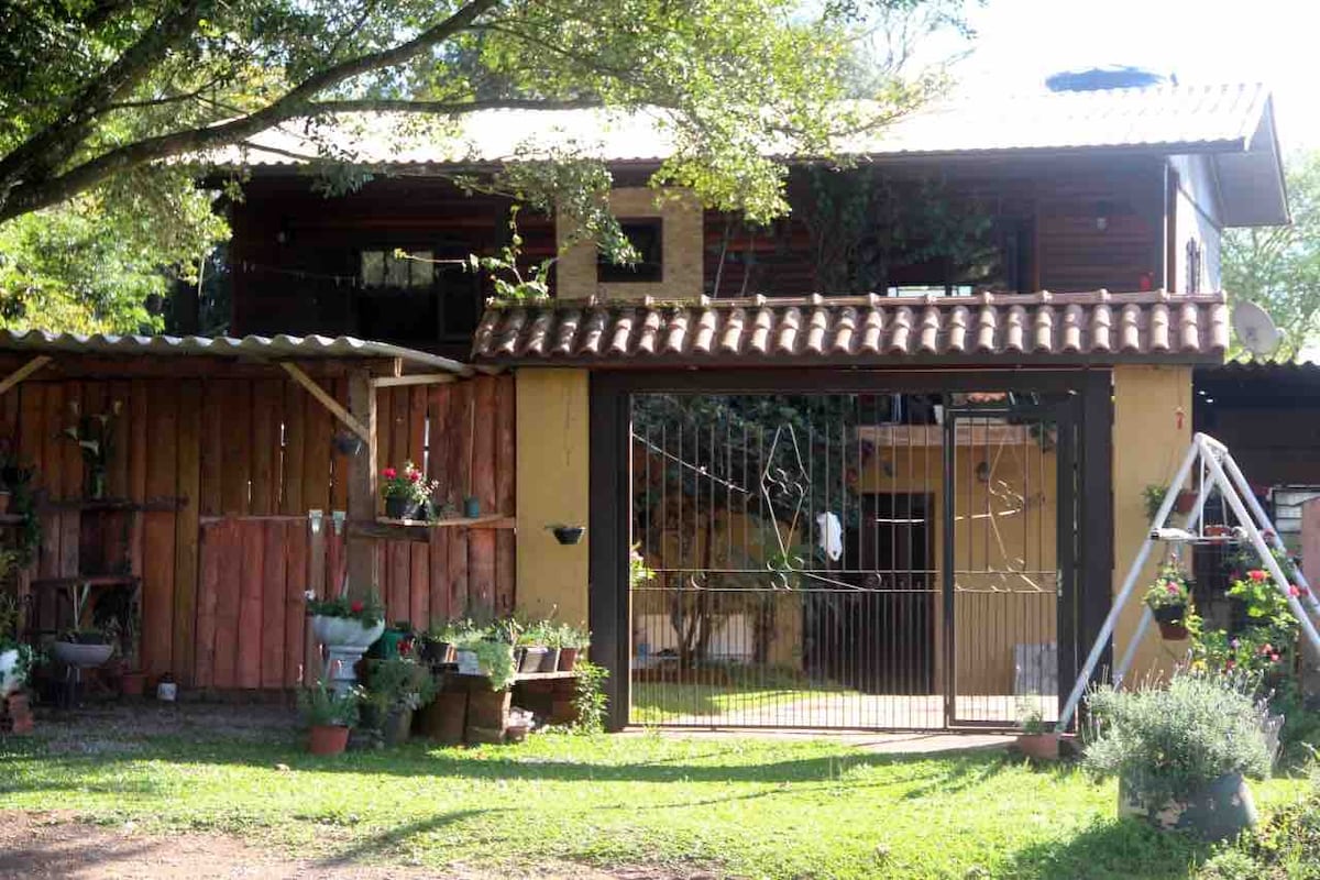 The exterior features a charming two-story building with a traditional tiled roof. A fenced garden area is visible, adorned with potted plants and colorful flowers. A wooden structure with decorative elements enhances the outdoor space, providing a welcoming entrance to the property.