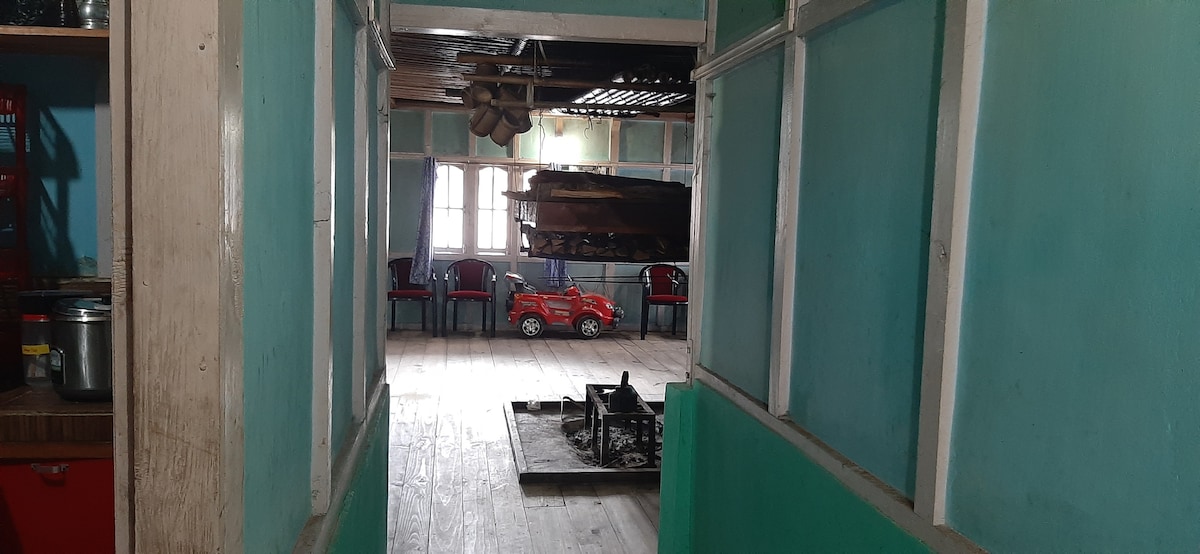 A corridor is presented, featuring walls painted in a calming green color. Wooden flooring is visible, leading towards a spacious room with chairs arranged in the background. A small red toy vehicle is placed on the floor, adding a touch of color to the space.