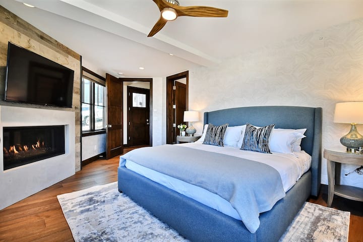 Primary King Bedroom Suite w/ private bathroom, fireplace, desk w/ chair, and large flatscreen TV.