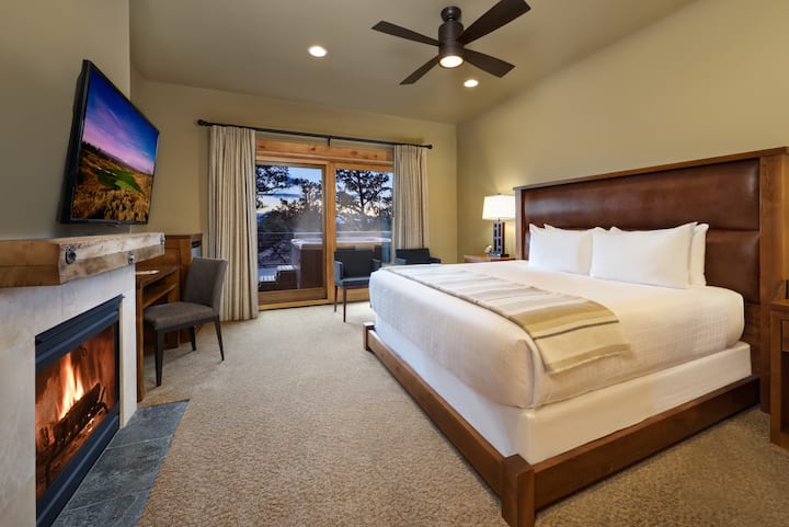 Bedroom 1 - Equipped with a plush king bed, gas fireplace, workstation, closet for storage, a small seating area, flatscreen TV, an en-suite bathroom, and back patio access. 