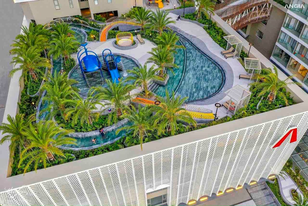 A landscaped pool area is visible, featuring a winding water slide, lush palm trees, and colorful play structures. The pool is surrounded by vibrant tile work and lounge chairs, creating a playful yet serene environment.