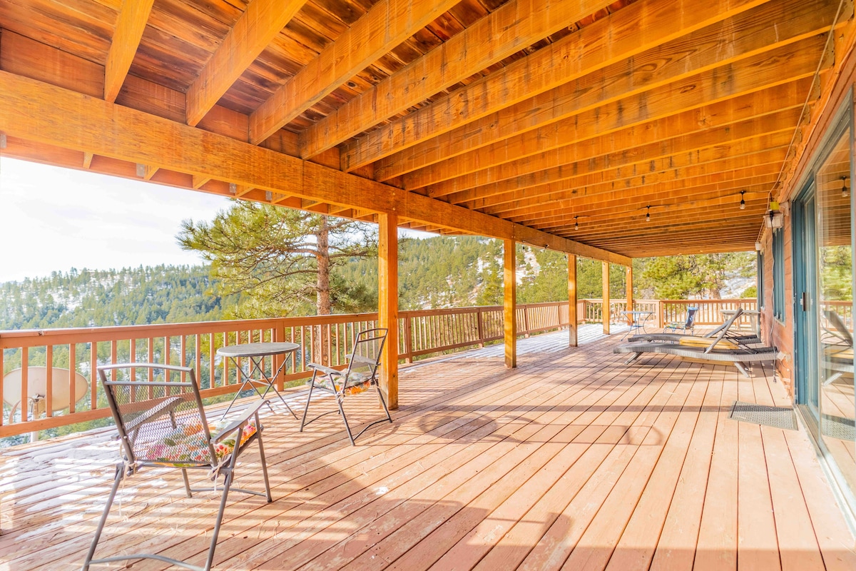 A spacious wooden deck is featured, offering unobstructed views of the surrounding mountainous landscape. Several lounge chairs are positioned for relaxation, while area is bathed in natural sunlight, creating a bright, inviting environment for outdoor enjoyment.