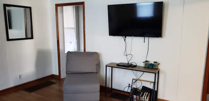 Ako je potrebno, TV se naginje 50".  Prijenos putem servisa Xfinity ili gledanje filmova iz naše kolekcije DVD-ova.  Stolić za kavu podiže se za hranu ili radnu visinu iz udobnosti kauča.

Otvaranje vrata s lijeve strane vodi do stepenica koje vode na kat ili preko glavne spavaće sobe .