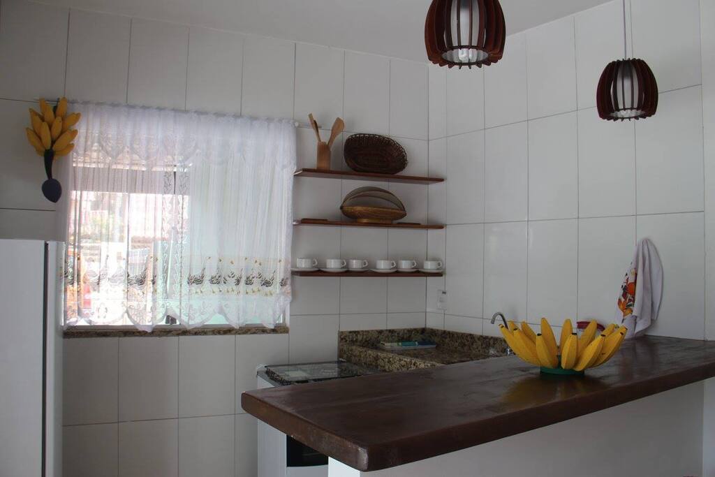 Cozinha equipada com fogão, geladeira, torradeira, liquidificador, cafeteira, louça, talheres e jogo de panelas.