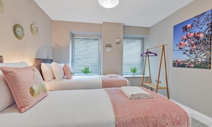 - ห้องนอนเตียงแฝดเงียบสงบเน้นสีชมพูอ่อนและเครื่องนอนที่อบอุ่นเพื่อบรรยากาศที่ผ่อนคลาย
- แสงธรรมชาติส่องเข้ามาในห้องเสริมด้วยศิลปะตกแต่งผนังและต้นไม้เขียวขจี
- การตกแต่งอย่างพิถีพิถันเช่นราวแขวนผ้าและกระจกช่วยเพิ่มความสะดวกสบายและมีสไตล์