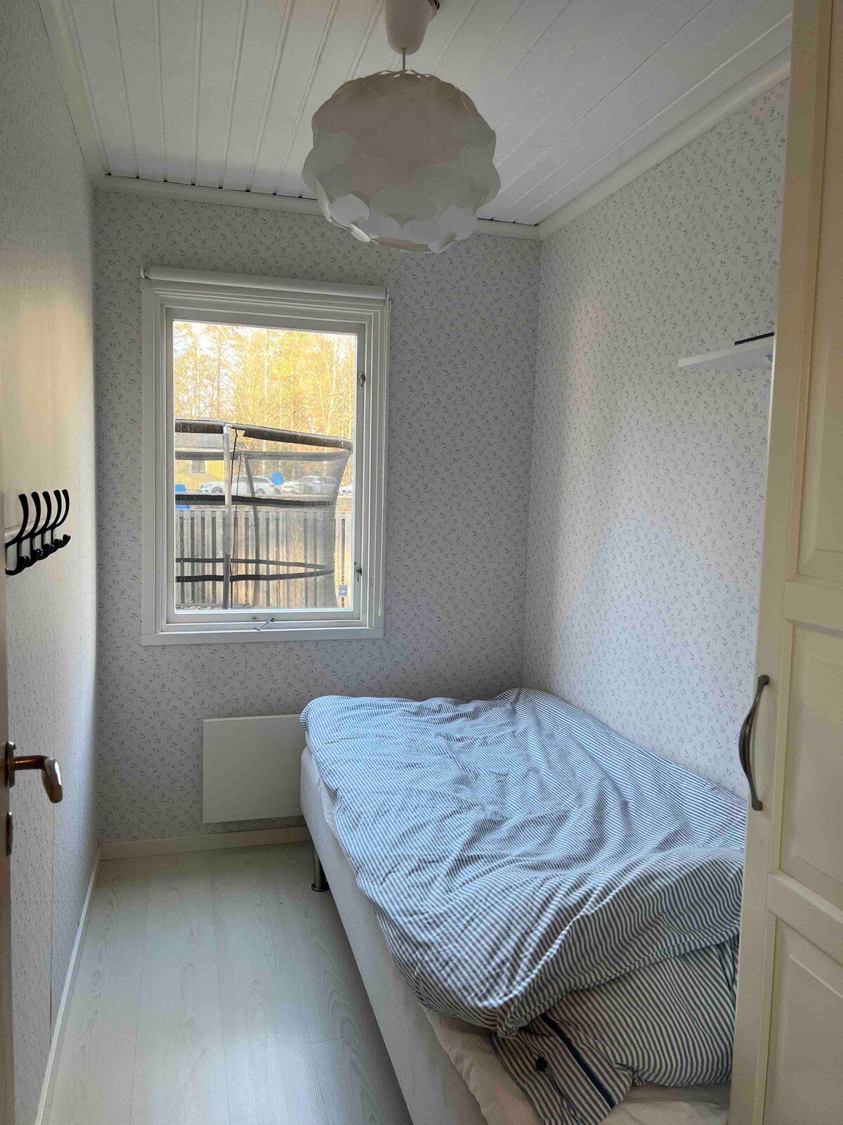 חדר שינה קטן עם 90 מיטות וארון בגדים. בחוץ, ניתן לראות את הטרמפולינה. 