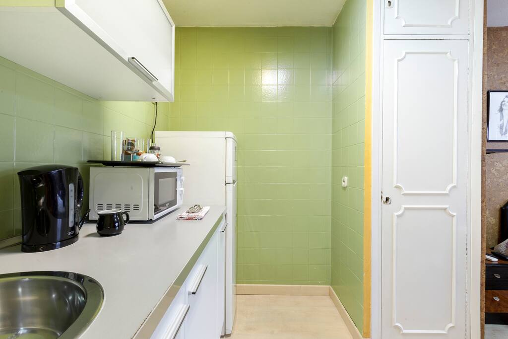 Pequeña cocina con frigorífico, microondas y calentador de agua.