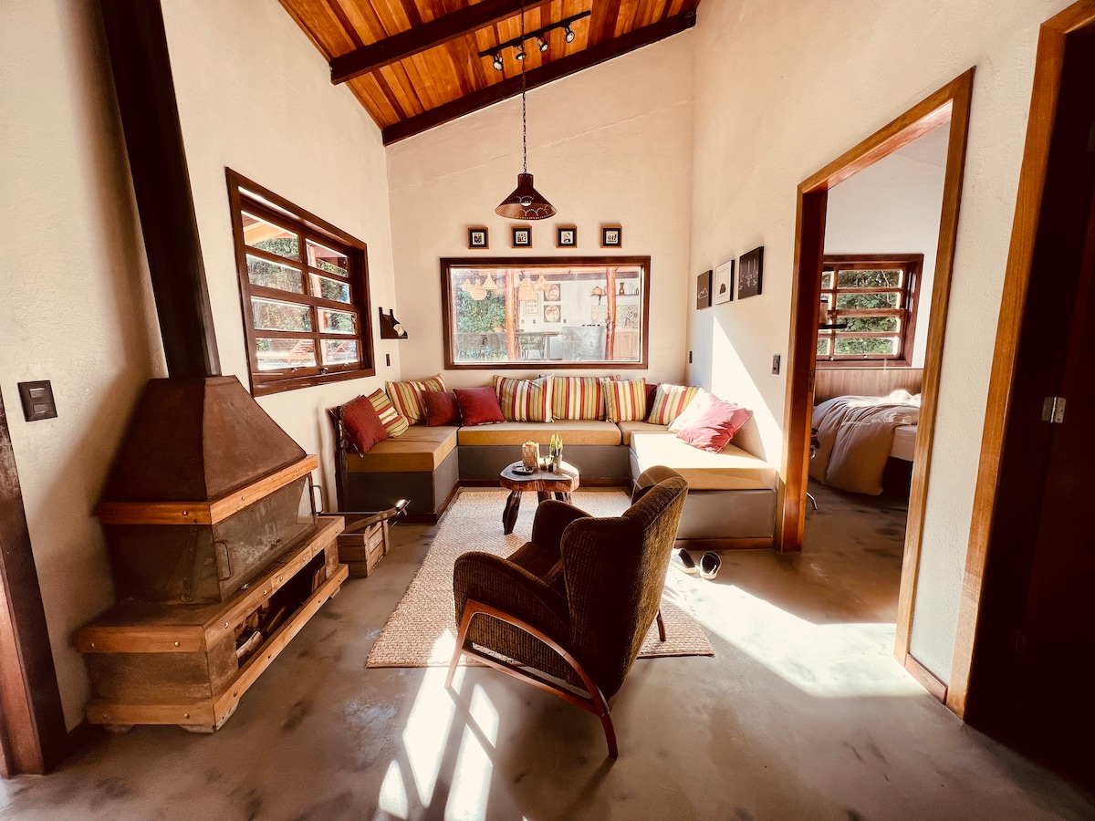 A spacious living area features a cozy sectional sofa adorned with colorful cushions, providing ample seating. Natural light streams through multiple windows, highlighting the rustic details. A wood-burning stove sits near the seating area, while warm wood accents enhance the inviting ambiance.