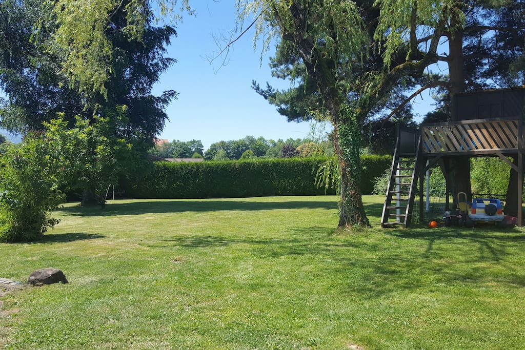 Grand espace vert avec cabane dans les arbres, toboggan et jeux pour enfants