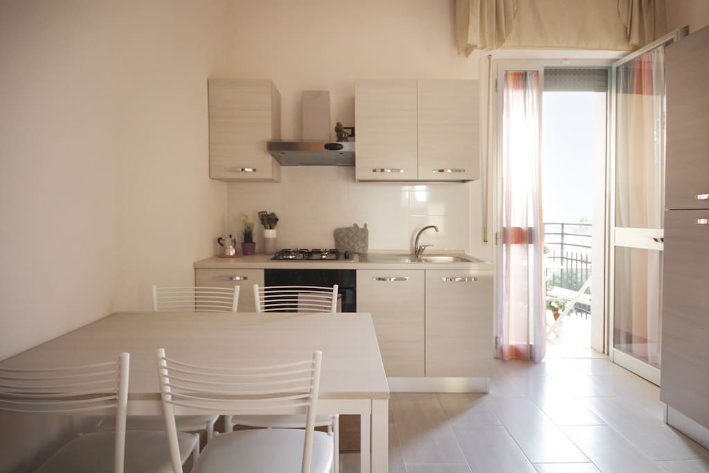 Soggiorno con tavolo e angolo cottura e balconcino.