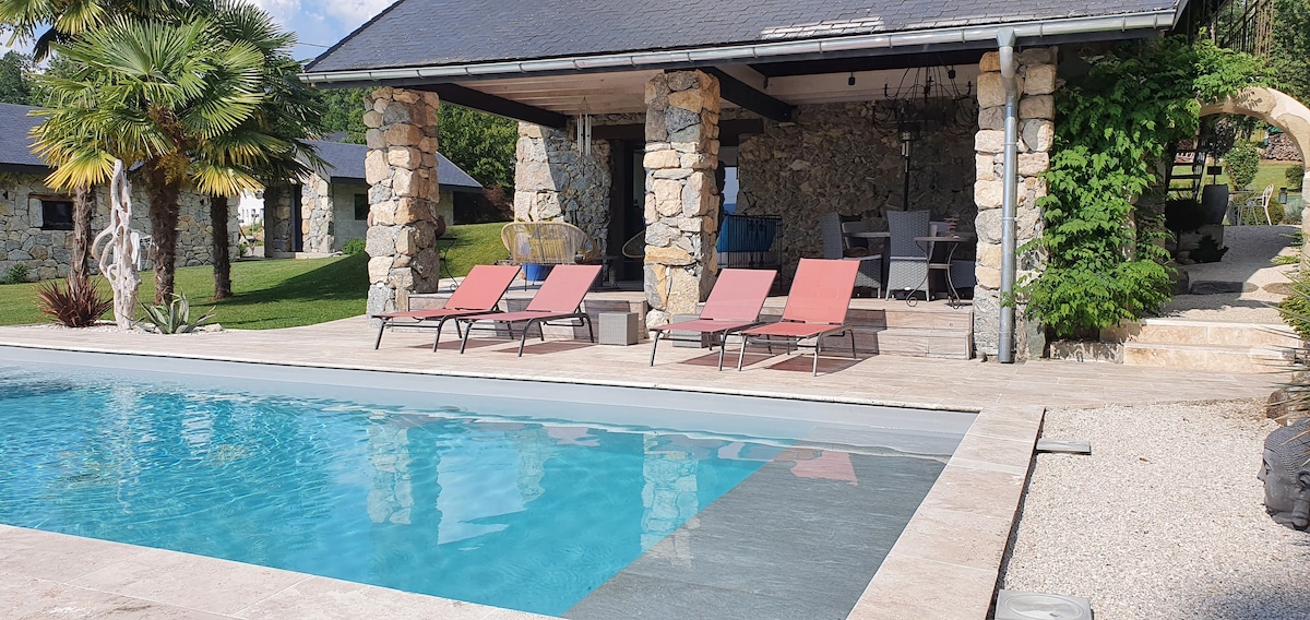 A serene outdoor area features a clear swimming pool bordered by a spacious terrace. Loungers are arranged for relaxation, while a covered seating space is adorned with stone walls and greenery, providing a welcoming environment for leisure.