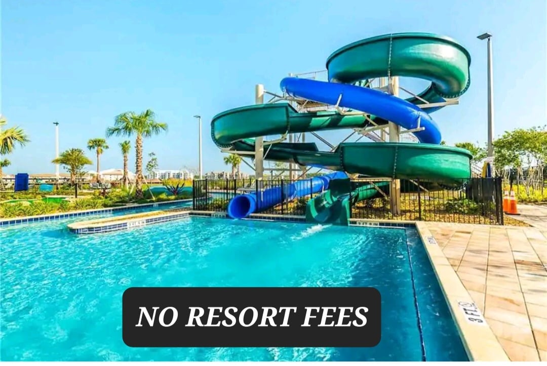 A resort-style pool area is featured, complemented by blue water slides curving toward the pool. Sunlight reflects off the water, enhancing the inviting atmosphere. Lush palm trees are visible around the pool deck, adding to the outdoor setting.