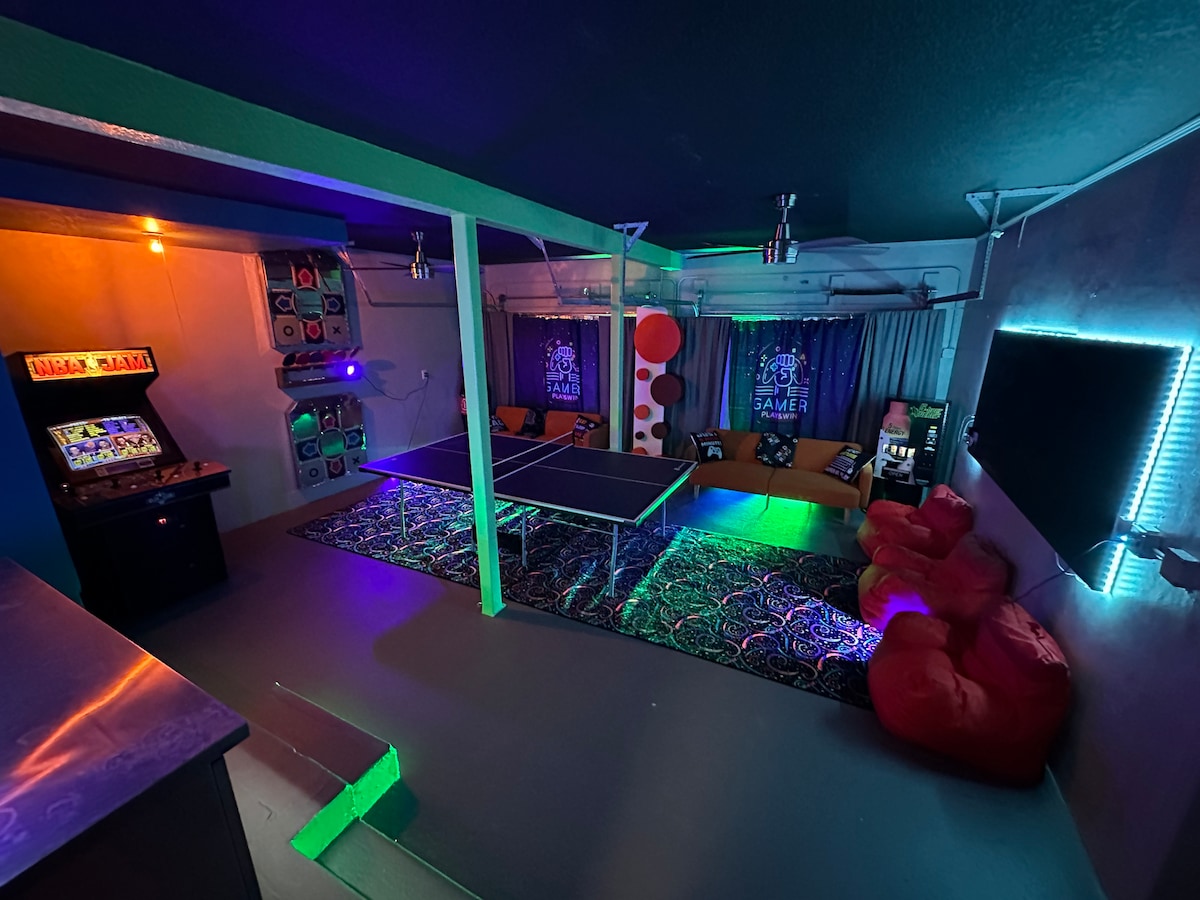 A vibrant game room is equipped with a ping pong table, cozy bean bag chairs, and arcade machines. The walls are adorned with colorful lighting and posters, creating an energetic atmosphere ideal for entertainment and relaxation.
