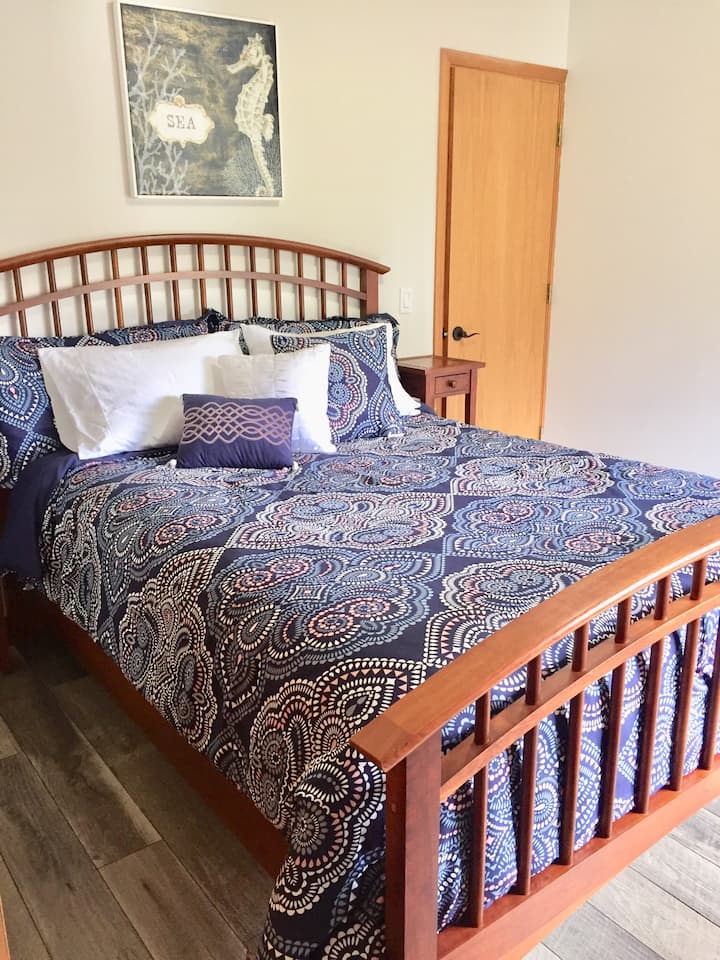 Downstairs bedroom with a queen bed, TV, and tower fan.