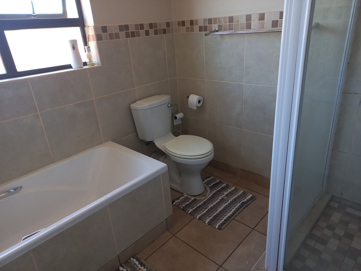 A well-equipped bathroom features a bathtub and a shower stall alongside a toilet. Neutral tile tones are complemented by a decorative border. Natural light enters through a window, enhancing the clean and functional layout.