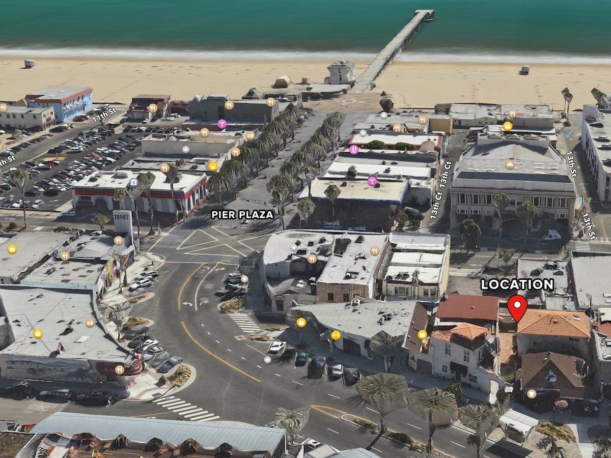 An aerial view of downtown Hermosa Beach captures the proximity to the beach and pier. The layout highlights nearby streets, shops, and the beach area, showcasing a vibrant community. Various buildings and parking areas are discernible, emphasizing easy access to beachside amenities.