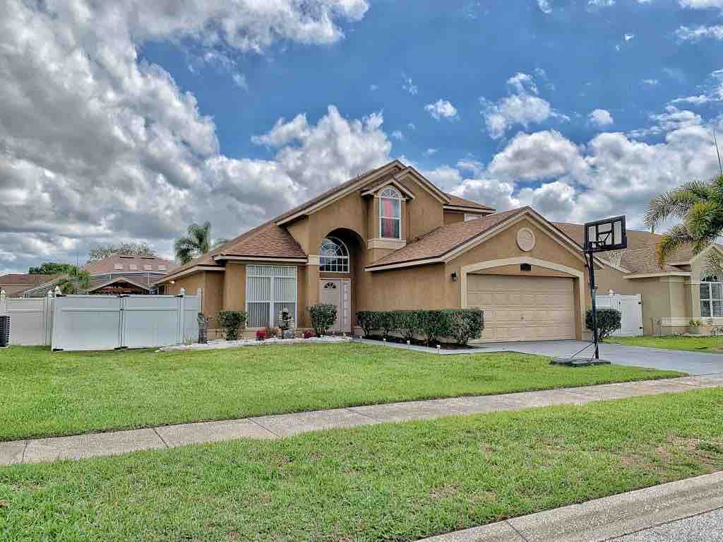 The exterior of the home showcases a charming, single-story structure with a peaked roof and a two-car garage. A well-manicured front lawn with neatly trimmed shrubs lines the walkway. Clear blue skies with scattered clouds create a vibrant backdrop.
