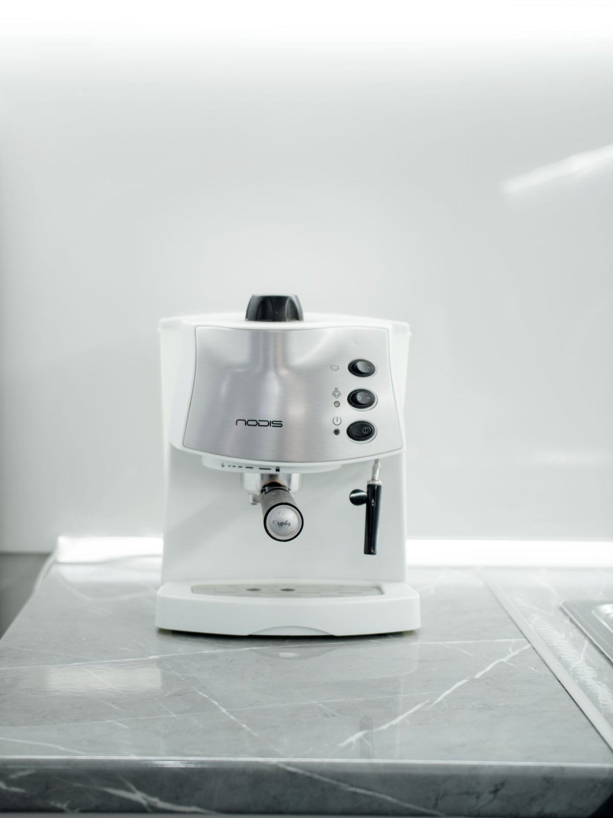A sleek white espresso machine is prominently displayed on a polished gray countertop. The machine features a silver body with control buttons and a coffee spout, showcasing a modern and functional design ideal for preparing fresh coffee.