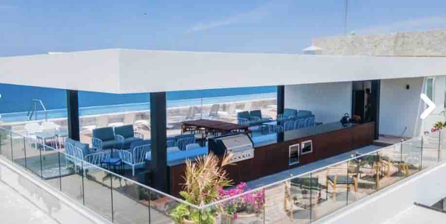 A spacious rooftop oasis is showcased, featuring a large grilling area surrounded by comfortable seating. Lounge chairs are positioned around a heated lap pool, offering panoramic views of the ocean. Lush greenery adds a touch of nature to this modern, relaxing space.