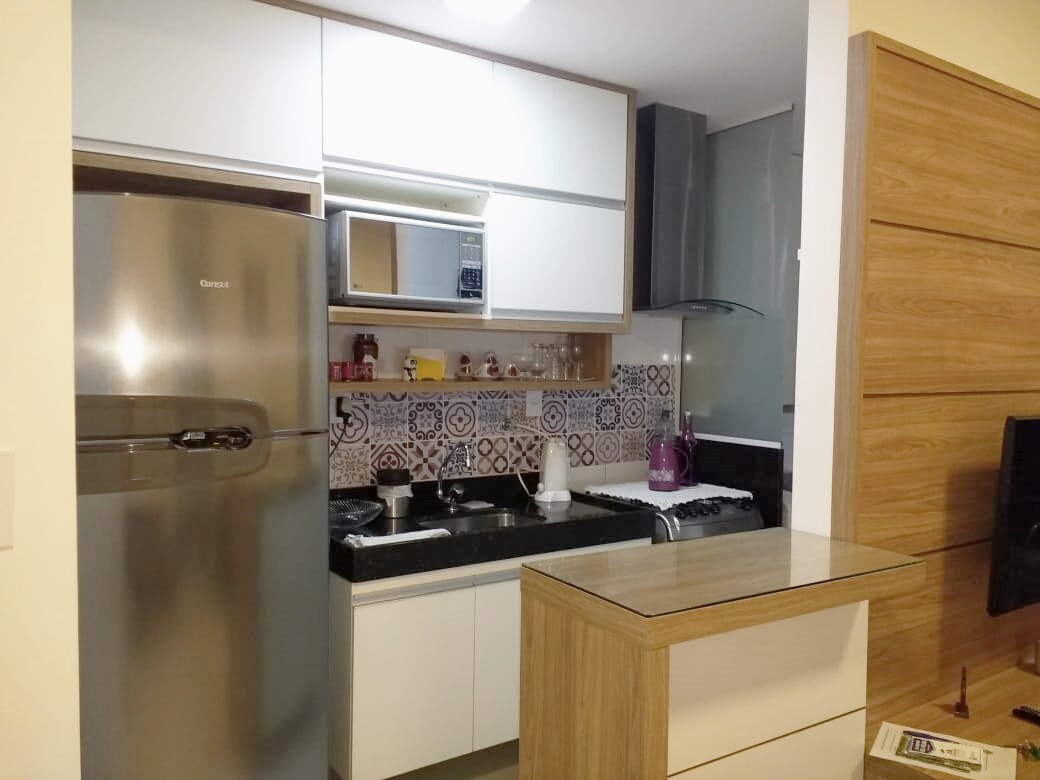 A compact kitchen area is presented, featuring modern appliances including a stainless steel refrigerator and a cooktop. The countertop provides space for food preparation, while decorative tiles add a subtle design element to the backsplash. Storage cabinets are neatly integrated into the space.