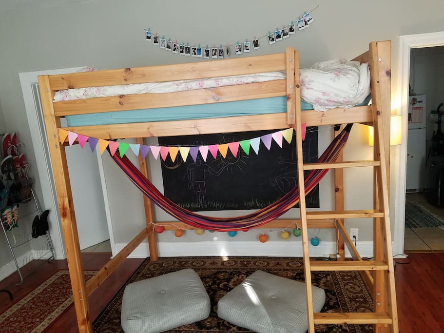 Lofted bed with hammock underneath and floor pillows