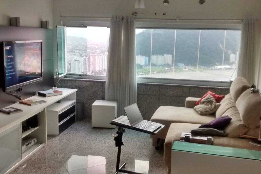 Grande sala conjugada com cozinha americana planejada com ampla vista por janelão blindex tipo 'camarão'.