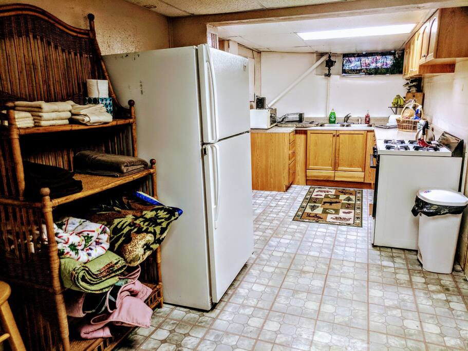 View of kitchen and its amenities: refrigerator, stove/oven, microwave. Also shown is linen rack for towels, bedding, and pillows.