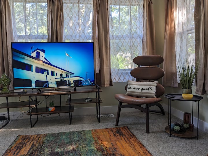 غرفة المعيشة خفيفة ومتجددة الهواء مع جدران كاملة من النوافذ. يوجد مصباح مصباح مروحة سقف علوية.  الكرسي الجانبي غير التقليدي مريح للغاية. 